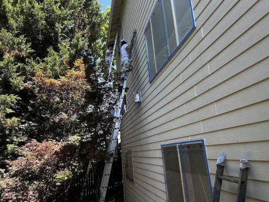 In July 2025, painters on ladders paint a beige Jennings house; Pearl Painters cover windows with tape and plastic.