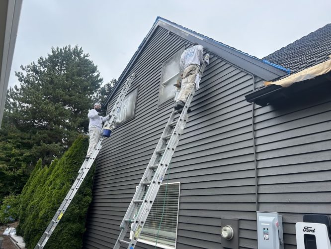 Painters Renee & Seamus Barron paint a home's upper wall near windows on ladders, Portland, August 2025, Pearl Painters.