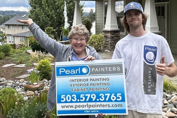 Two people stand in front of a house, holding a sign for "Pearl Painters" offering interior, exterior, and cabinet painting services, with contact information and website URL included.