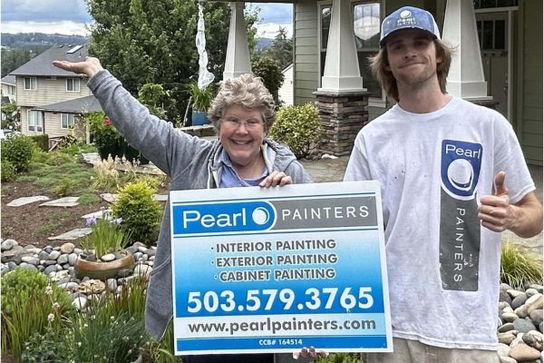 Two people stand in front of a house, holding a sign for "Pearl Painters" offering interior, exterior, and cabinet painting services, with contact information and website URL included.