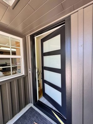 A painter from Pearl Painters in Portland painted a modern Mastalir exterior front door with horizontal frosted glass panels, partially open beside a window with shelves inside, for a May 2025 project.