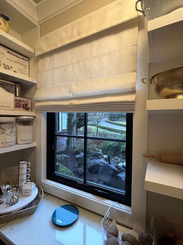 Interior pantry in Portland features shelves, a window with a white Roman shade, and kitchen items like a strainer, rolling pin, and McCormick scale overlooking the garden. Ideal painting inspiration for Pearl Painters in April 2025.