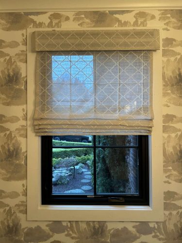 A painter in Portland completed a stylish interior with beige and gray abstract wallpaper (McCormick April 2025 collection) and a window with a patterned Roman shade overlooking a garden path. Pearl Painters did the painting.