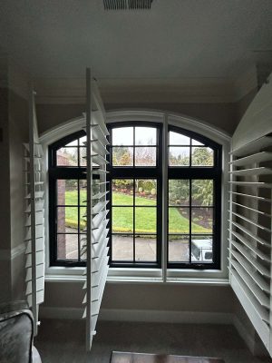 A large interior window with black grid panes and open white shutters at McCormick provides a view of the landscaped garden and lawn. Pearl Painters, a Portland painting company, highlights this peaceful setting in April 2025.
