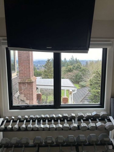 Pearl Painters completed interior painting in this McCormick, Portland home, where a row of dumbbells is placed before a window with an outdoor view and a large TV mounted above. (April 2025).