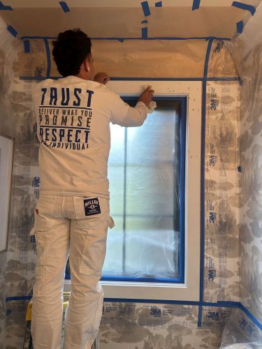 A painter from Pearl Painters prepares a McCormick-branded interior room for painting in Portland by taping protective paper around a window frame. Renovation is scheduled for April 2025.