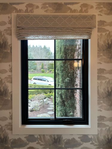 A window with a light gray roman shade overlooks a garden, paved path, shrubs, and a white vehicle at McCormick in April 2025. For painting needs in Portland, contact Pearl Painters.