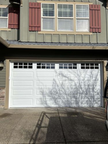 In April 2025, painter Taylor installed a closed white garage door with rectangular top windows on her green house with red shutters and a concrete driveway in Portland.
