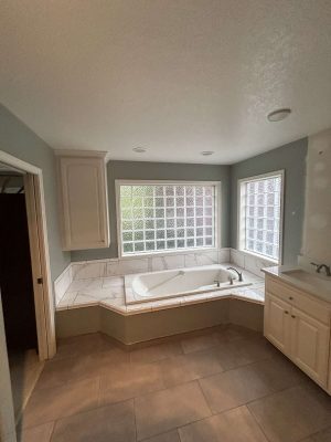Portland painter Pearl Painters recommends this updated bathroom: glass block windows, marble-surround bathtub, light cabinets, and tiled floors and walls—ideal for a Mallen home refresh in April 2025.