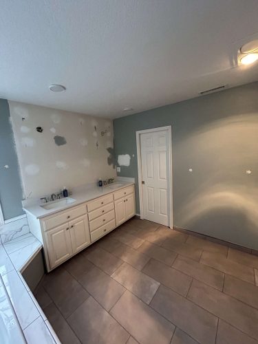 A bathroom in Portland by Pearl Painters shows tiled flooring, white cabinetry, and an unfinished wall with exposed drywall spots next to a closed white door.