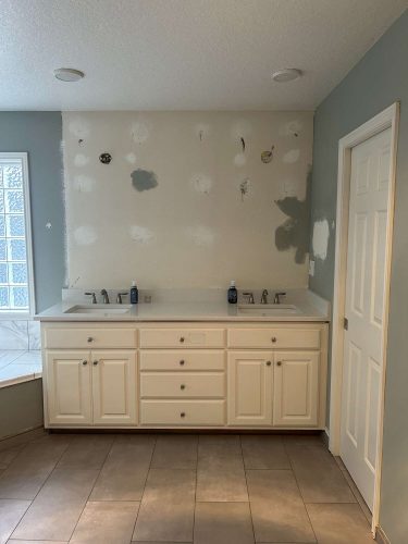 Bathroom with double-sink vanity, white cabinets, and light countertops. Unfinished wall patches show recent removal of mirrors or cabinets. Ready for updates and painter work by April 2025 in Mallen; contact Pearl Painters, serving Portland and beyond.