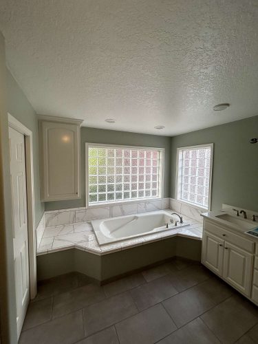 Spacious Mallen interior bathroom in Portland with white bathtub, glass block windows, light green walls, tile flooring, and white cabinetry. Pearl Painters can refresh this space in April 2025.