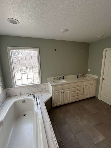 A Mallen interior bathroom in Portland with a white bathtub, tiled floor, double-sink vanity, and frosted glass window. Ideal for April 2025 painting updates by Pearl Painters.