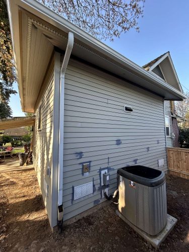 Exterior side view of a Congdon house in Portland, showing light gray siding with patch spots, outdoor AC unit, and utility connections in April 2025. Painting work by Pearl Painters.