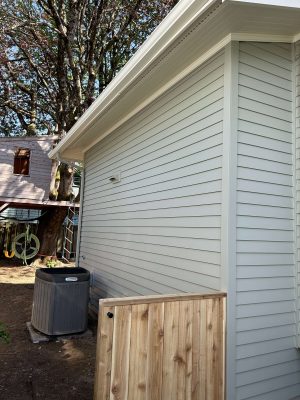 A light gray vinyl-sided Congdon house in Portland with a wooden gate, exterior AC unit, and trees. Painted by Pearl Painters. Photo: April 2025.