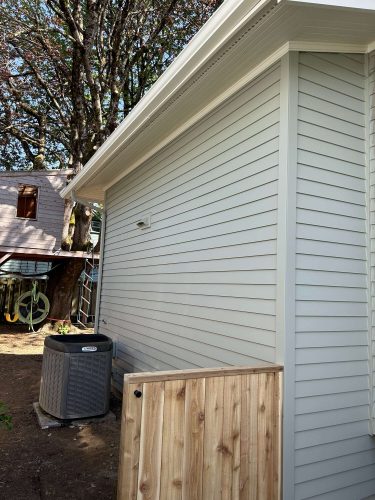 A light gray vinyl-sided Congdon house in Portland with a wooden gate, exterior AC unit, and trees. Painted by Pearl Painters. Photo: April 2025.