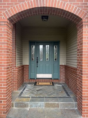 A brick and gray stone entryway in Portland features a green front door with glass panels. Pearl Painters can help paint your exterior for a fresh look this April 2025.