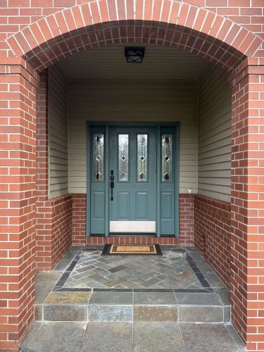 A brick and gray stone entryway in Portland features a green front door with glass panels. Pearl Painters can help paint your exterior for a fresh look this April 2025.