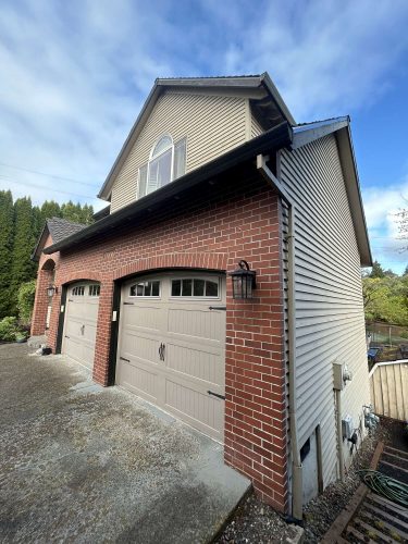 A two-story house in Portland features beige siding and a brick facade, with tan garage doors. Photo taken in April 2025. Painted by Pearl Painters.