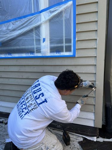 Painter Scott, of Pearl Painters in Portland, repairs exterior siding on a house covered with protective plastic and tape in April 2025.