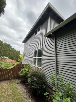 Photo of a gray two-story house in Portland with a wooden fence and shrubs, taken by painter Scott of Pearl Painters in April 2025.