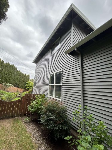 Photo of a gray two-story house in Portland with a wooden fence and shrubs, taken by painter Scott of Pearl Painters in April 2025.