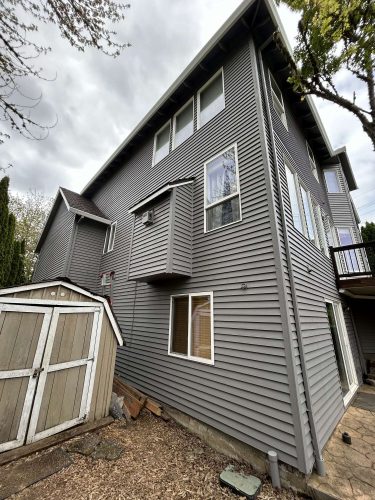 A gray three-story house with vinyl siding and multiple windows is shown under an overcast April 2025 sky in Scott. Pearl Painters, a Portland-area painting company, completed the exterior painting.