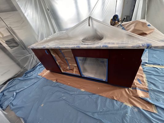 A wooden cabinet in Portland is prepped for painting by Pearl Painters, covered with plastic, tape, and surrounded by drop cloths.