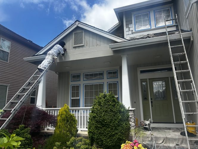 A painter from Pearl Painters is painting the exterior of a two-story house with green shrubs in front in Hendricks, as part of a renovation project scheduled for May 2025.
