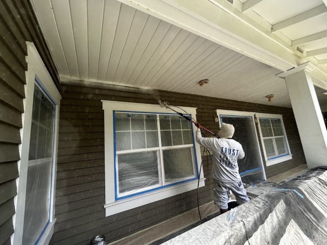 In June 2025, a painter from Pearl Painters uses a sprayer to paint a covered porch ceiling in Kearns; windows and surfaces are taped for protection.