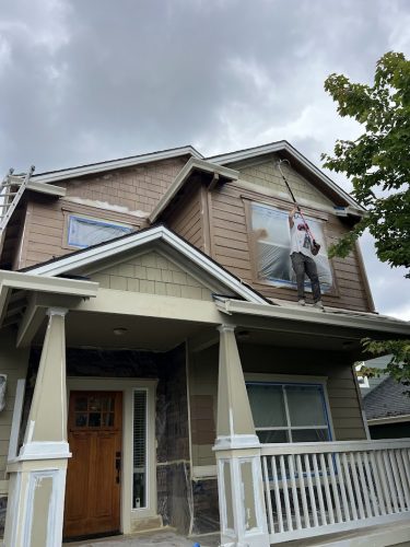In June 2025, a painter with Pearl Painters paints the upper level of an Emory house in Portland brown, covering windows and trim with plastic.