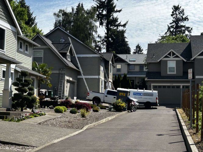 A white ProStar Painting van and a ladder are seen outside gray houses on a residential street in Austin. The scene shows painting work similar to that by companies like Pearl Painters in Portland.