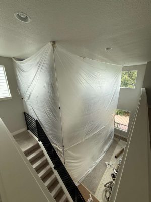 Plastic sheeting surrounds a stairwell in this Turk project in Portland, providing a barrier for painting and renovation. Tools and materials are on the floor below. Pearl Painters is scheduled to complete the work in May 2025.