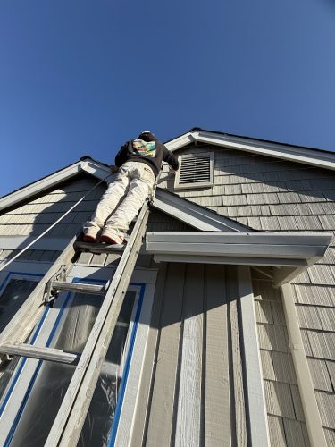 In May 2025, a painter from Pearl Painters works on the exterior near the attic vent of a Hendricks house in Portland.