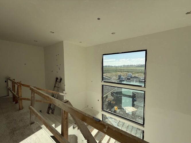 Interior of an unfinished room at Wheeler, Portland, painted white by Pearl Painters. Photo from June 2025 shows a wooden railing, ladder, and window overlooking parked vehicles and a field.