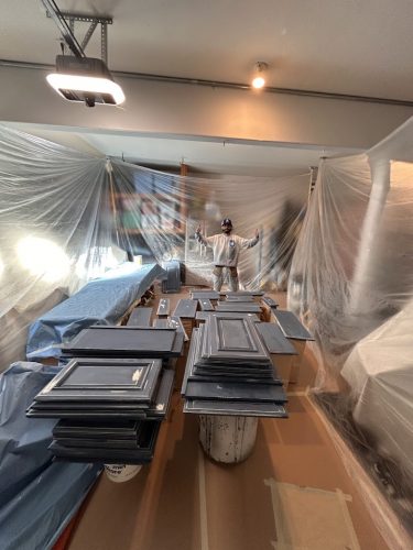A painter from Pearl Painters stands in protective gear in a plastic-covered room in Portland with painted cabinet parts drying.