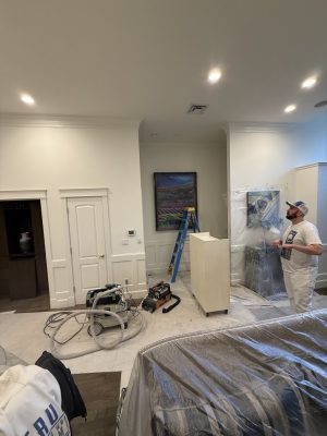 A painter from Pearl Painters stands in a plastic-covered Portland room with equipment, a ladder, and a painting on the wall.