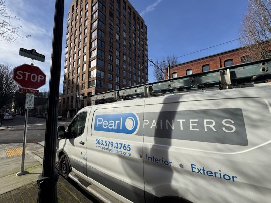 Pearl Painters van with ladder parked on Portland street by stop sign; tall brick building in background; painting service.