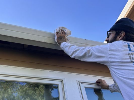 A painter in glasses and cap cleans window trim before painting for Pearl Painters on a house exterior in Portland.