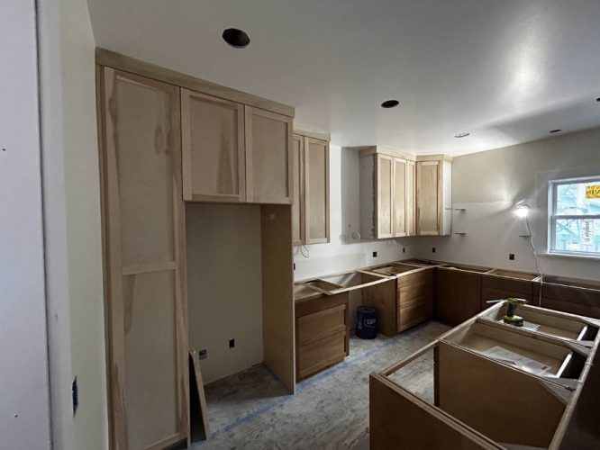 A kitchen under construction in Portland with unpainted wooden cabinets, recessed lighting, and a workspace table setup