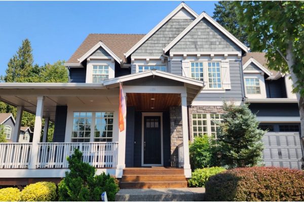 A gray house with a front porch and fresh bushes.