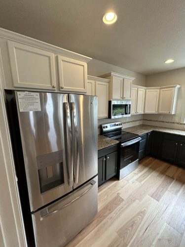 Kitchen in Rockaway Beach rental property, with white upper cabinets and dark grey blue lower cabinets, freshly painted