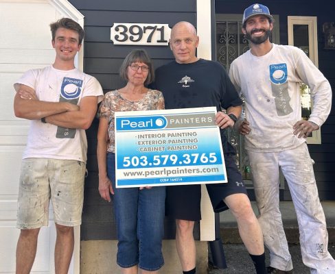 Four people in front of a house in Portland hold a Pearl Painters sign; two wear painting gear, others are casual and athletic.