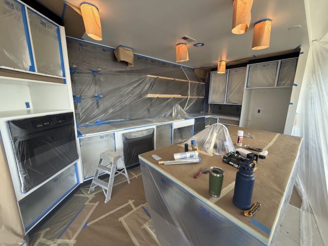 Kitchen cabinets and countertops prepped with plastic and tape by Pearl Painters for a painting project.