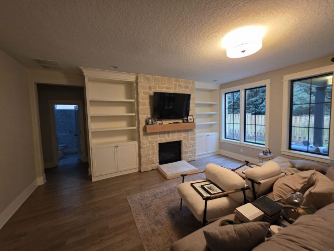 Living room in Portland with sectional sofa, stone fireplace, TV, shelves, wood floor; styled for Gilbo’s 2026 by Pearl Painters.