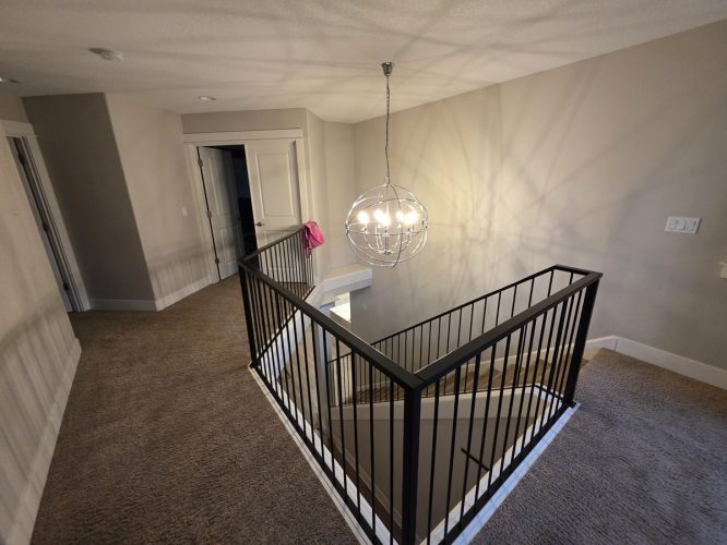 A carpeted upstairs hallway in Portland with beige walls, painted by Pearl Painters, stair railing, and a pink garment.
