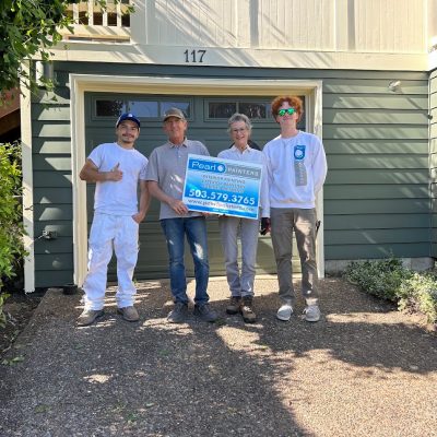 Four people stand in front of a green house with a "Pearl Painters" sign and house number 117, likely in Portland.