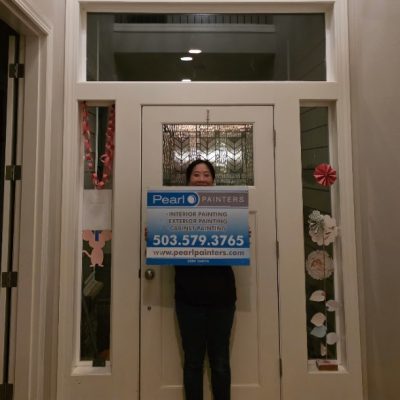 Person inside doorway holds Pearl Painters painting sign; paper decorations on nearby glass panels. Setting appears to be Portland.