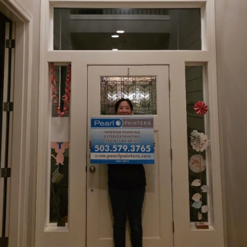 Person inside doorway holds Pearl Painters painting sign; paper decorations on nearby glass panels. Setting appears to be Portland.