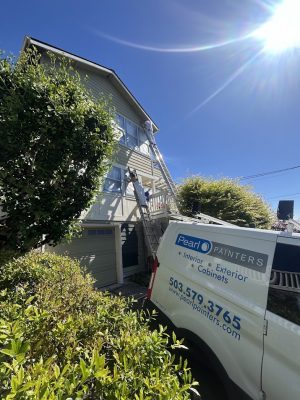 A painter on a ladder paints a house exterior in Portland as a Pearl Painters van is parked nearby.